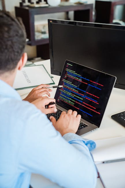 A photograph of a cluttered computer screen displaying lines of colourful computer code in various shades of black, red, green, yellow, blue, and white. The code consists of text, symbols, and numbers